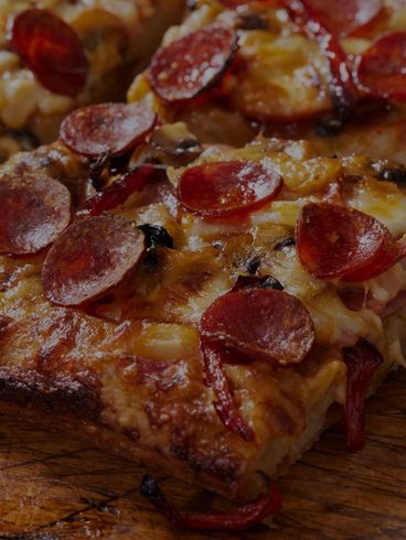 Pepperoni pizza slice, close-up with visible crust, cheese, and toppings on a wooden surface.