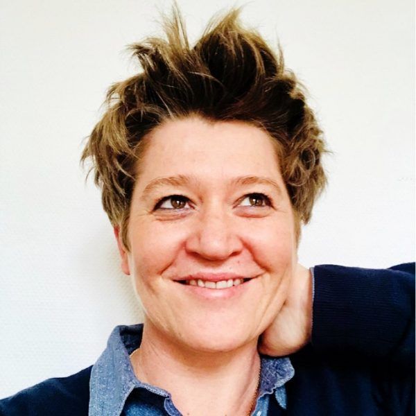 A woman with short hair is smiling with her hand on her neck
