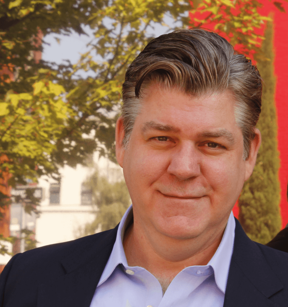 A man in a suit and blue shirt is smiling for the camera