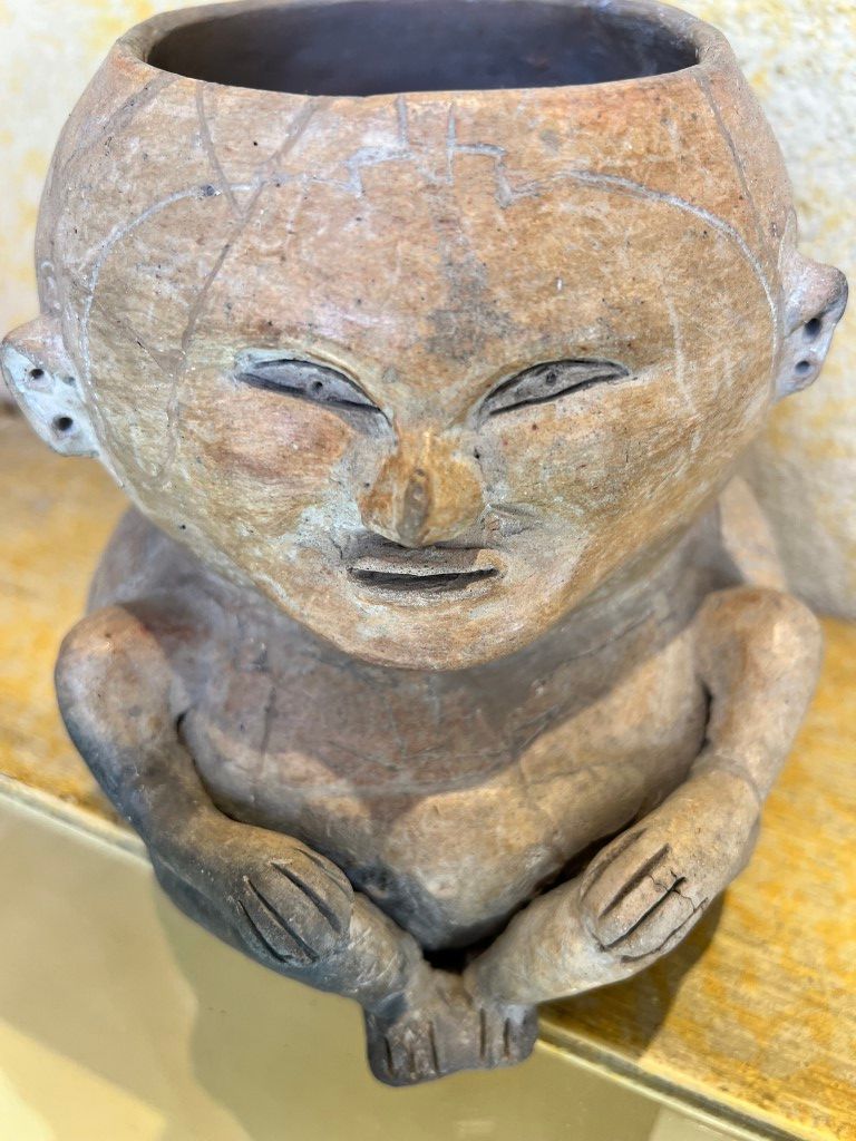 A clay vase with a face on it is sitting on a wooden table.