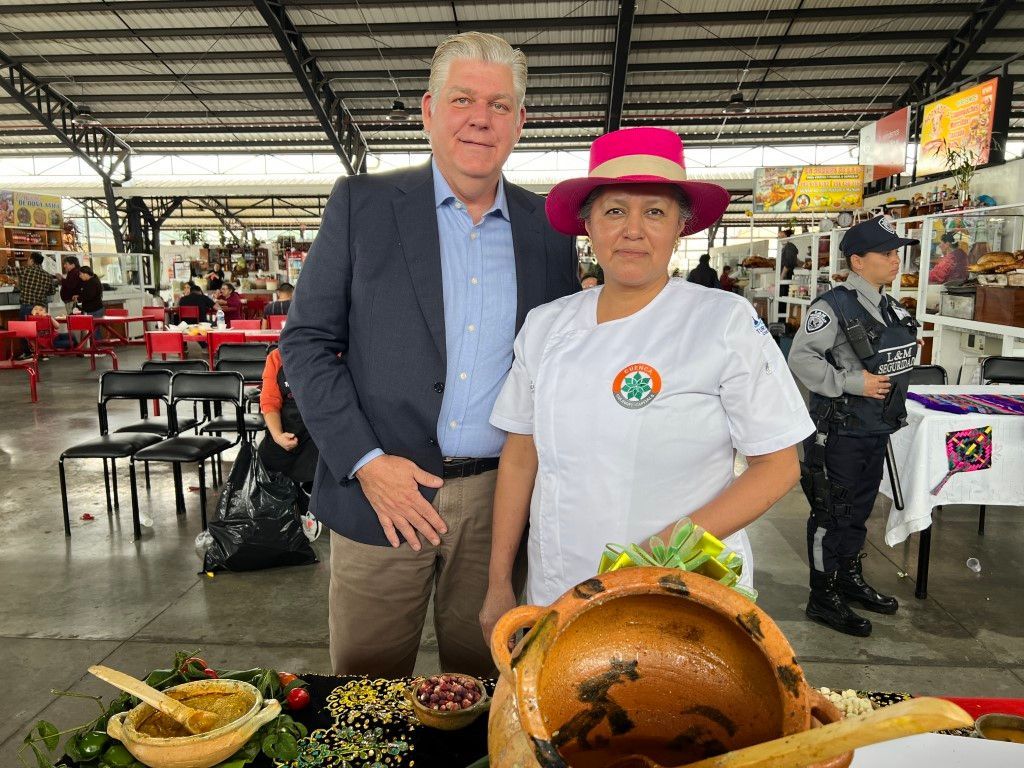 A man and a woman are posing for a picture in front of a pot of food.