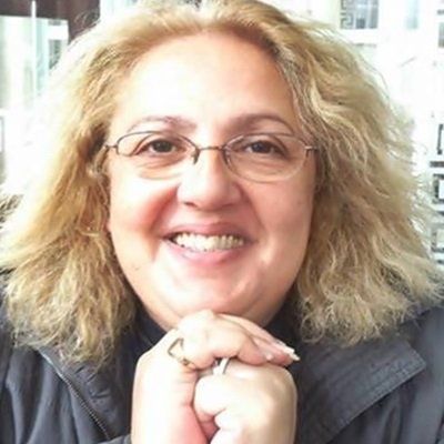 A woman wearing glasses is smiling with her hands folded