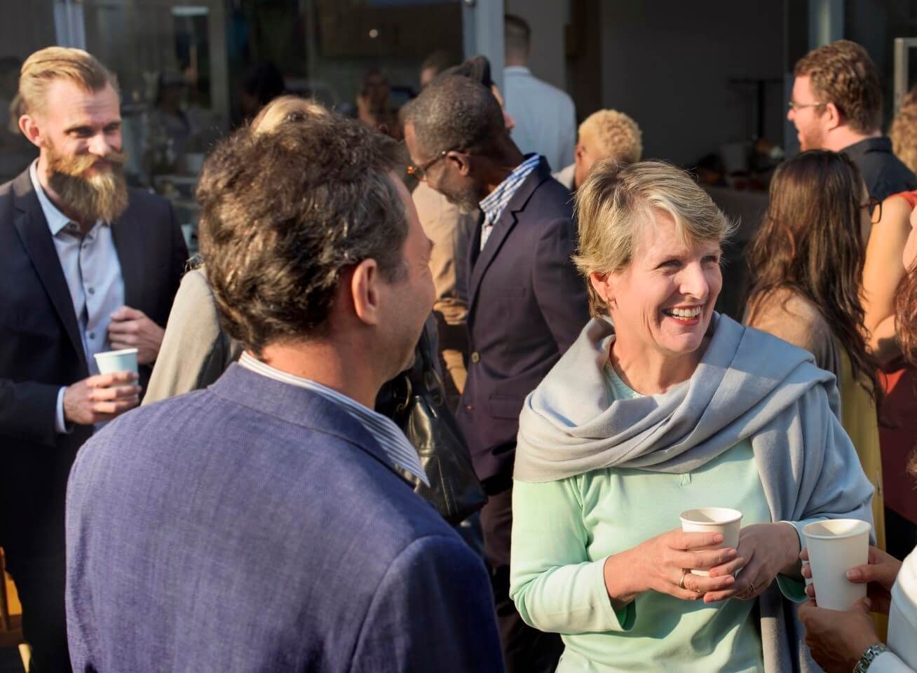 A group of people are standing around talking and drinking coffee.