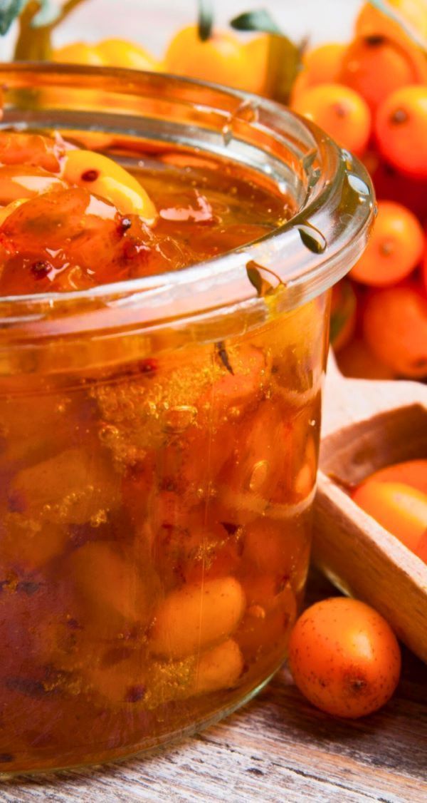 A glass jar filled with a sauce next to a bowl of fruit.