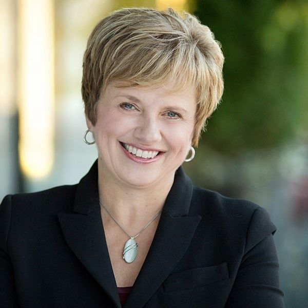 A woman wearing a black jacket and necklace smiles for the camera