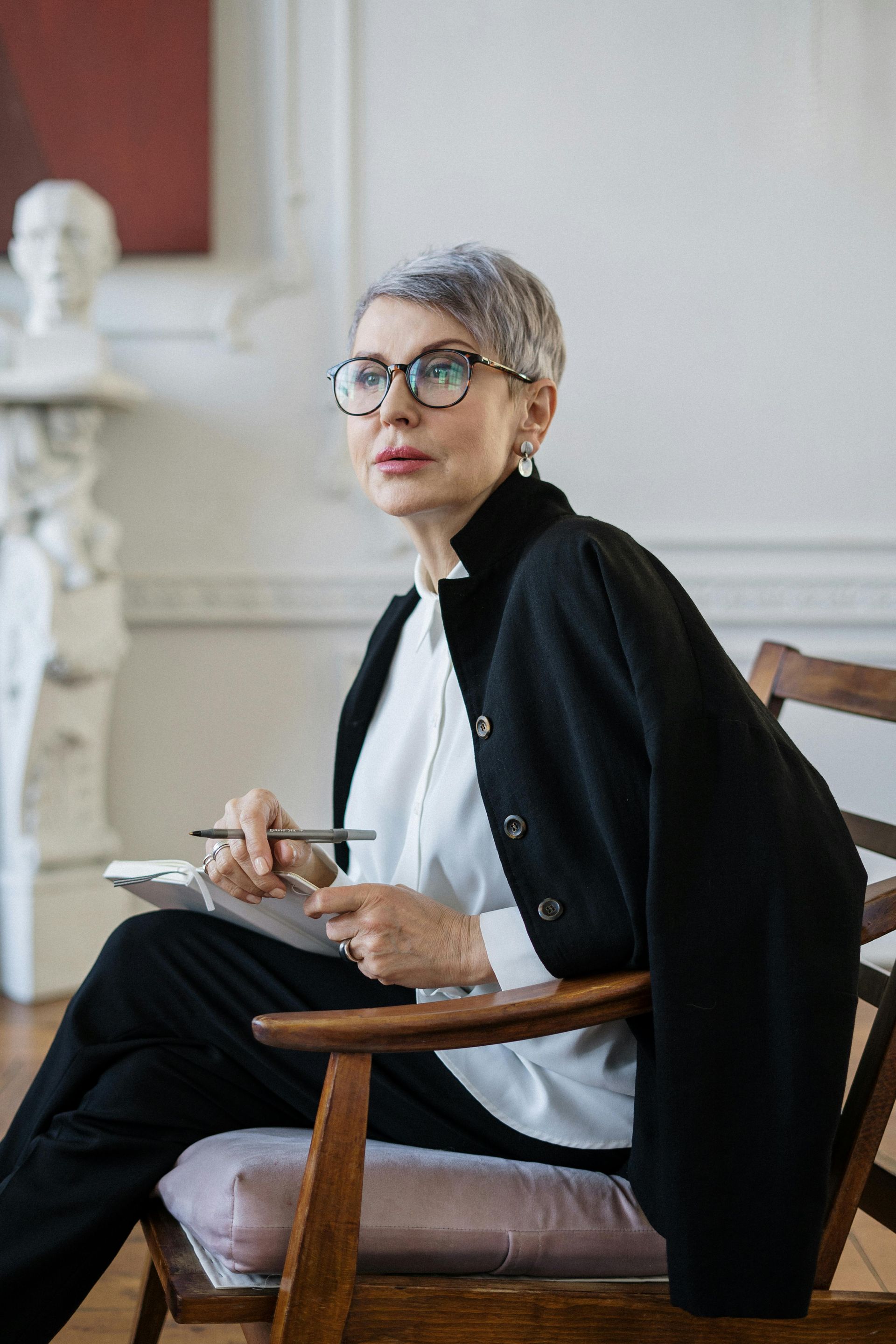 A woman is sitting in a chair holding a pen and a clipboard.