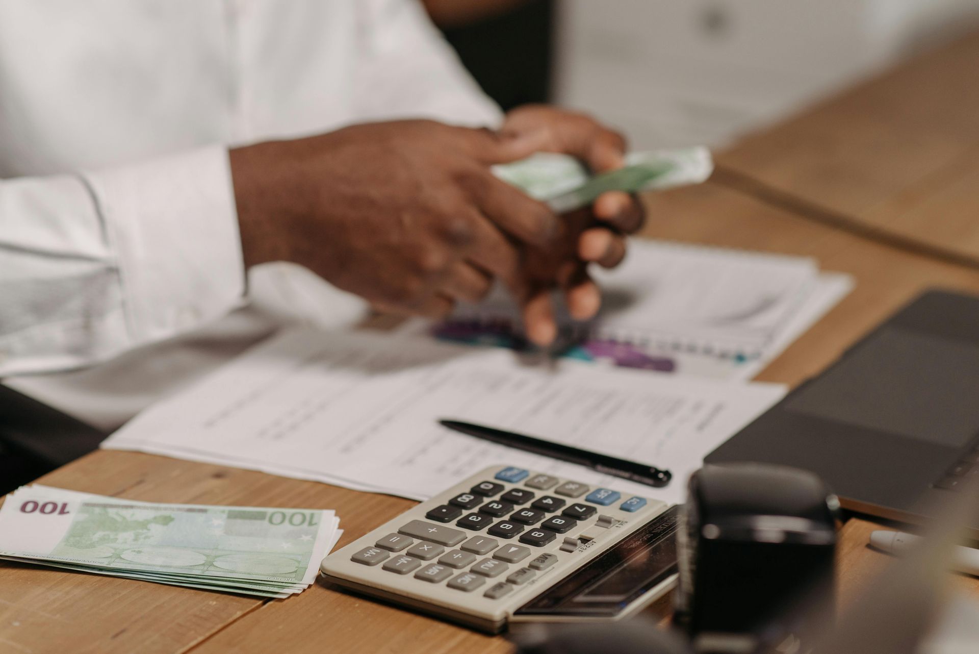 A man is sitting at a desk counting money and using a calculator.