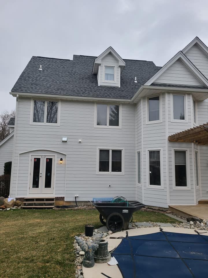A large white house with a gray roof and a pool in the backyard.
