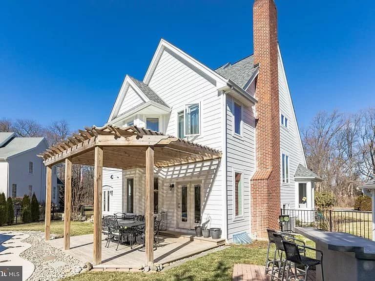 The back of a white house with a pergola and a brick chimney.