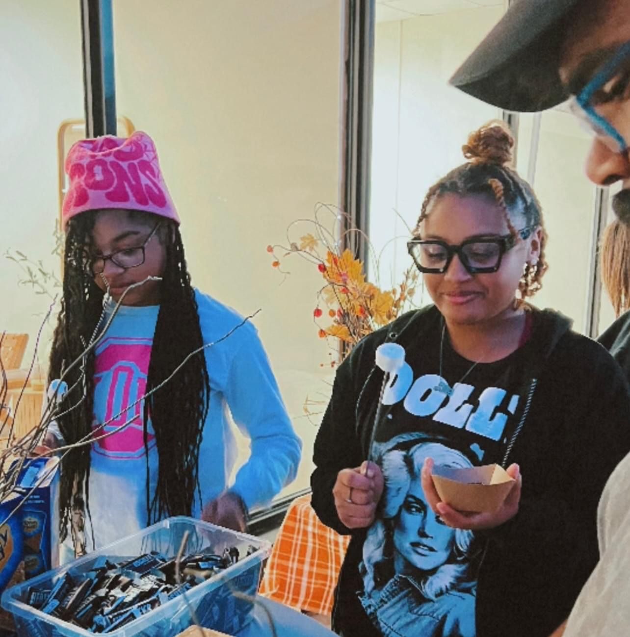 Two people, one in a pink hat, the other in glasses, work at a table with materials.