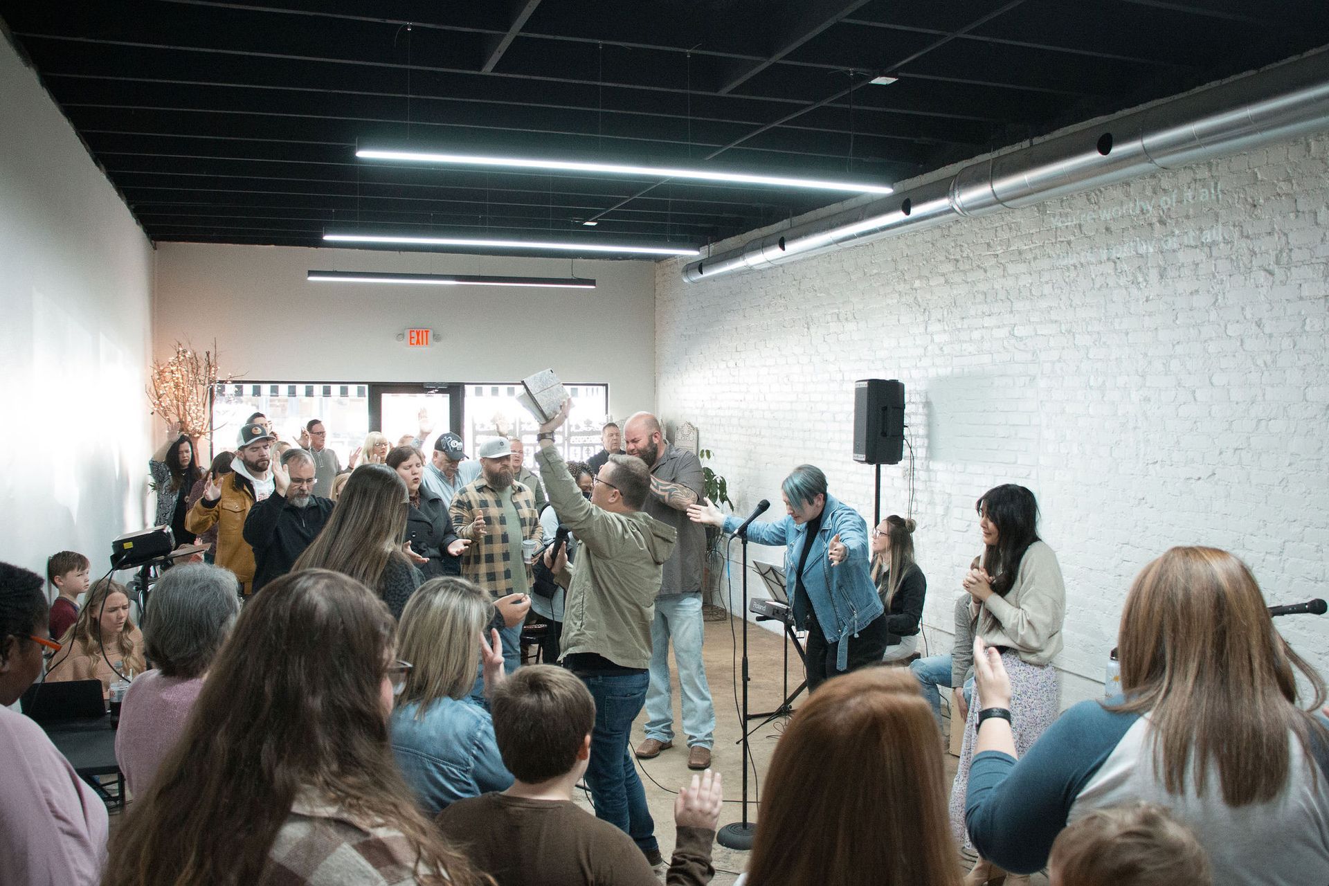 People gathered in a modern room, a person holding up a book, others listening, microphones and a speaker present.