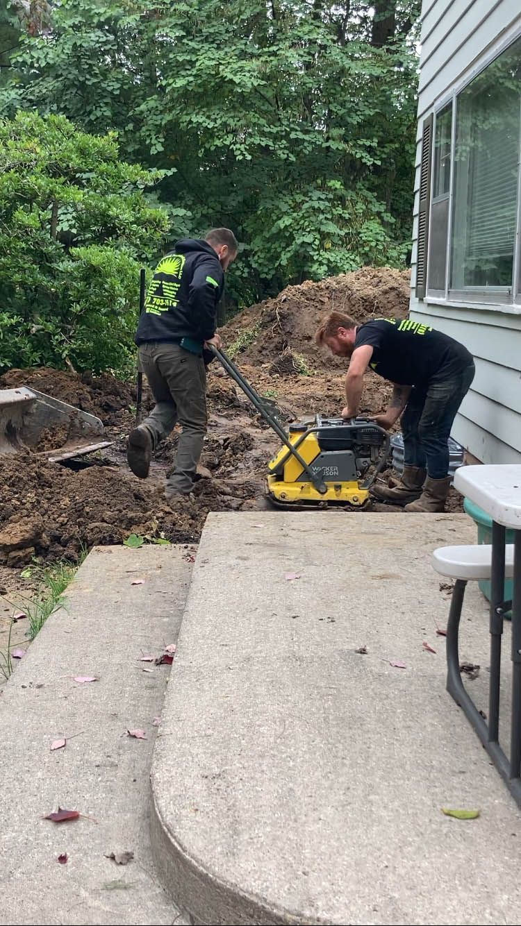 Two men are digging in the dirt in front of a house.