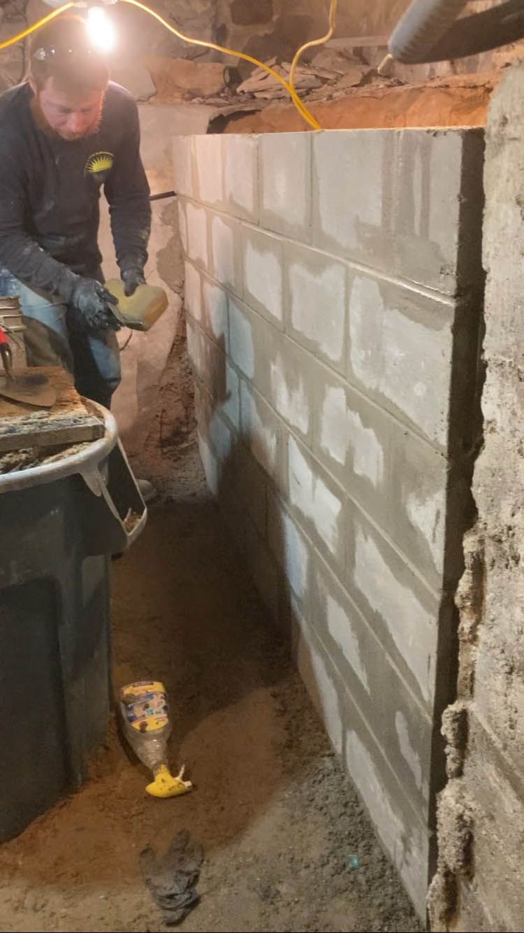 A man is working on a brick wall in a basement.