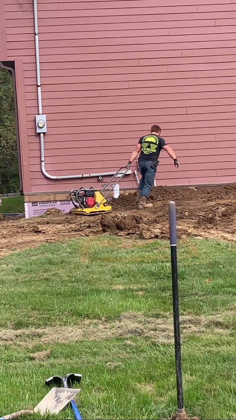 A man is digging a hole in the dirt in front of a house.