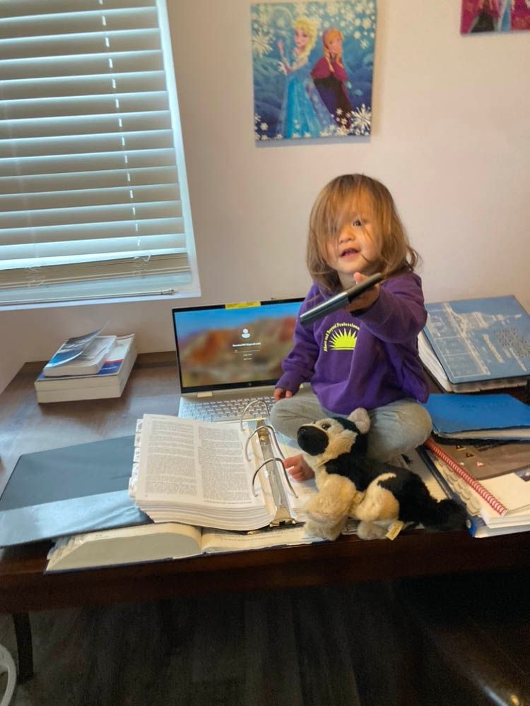 A little girl is sitting on a desk with a book and a stuffed animal