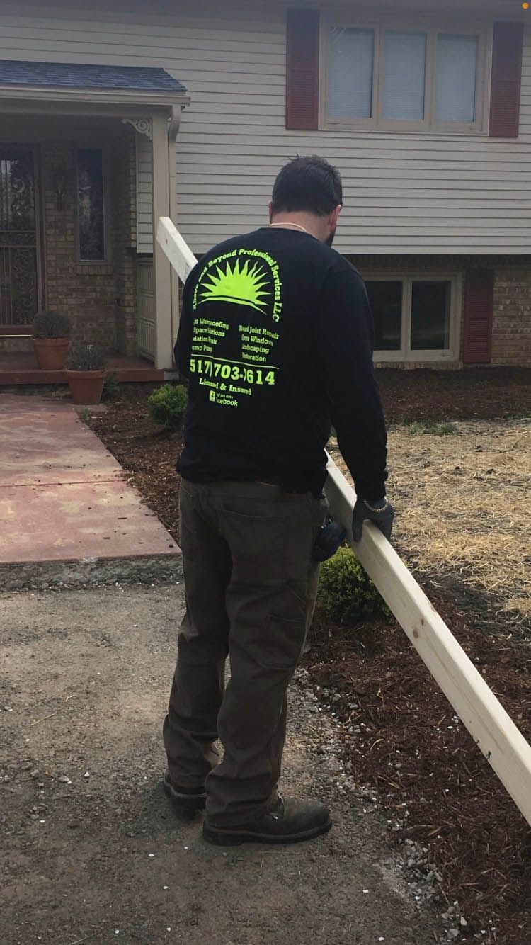 A man in a black shirt is holding a piece of wood in front of a house.