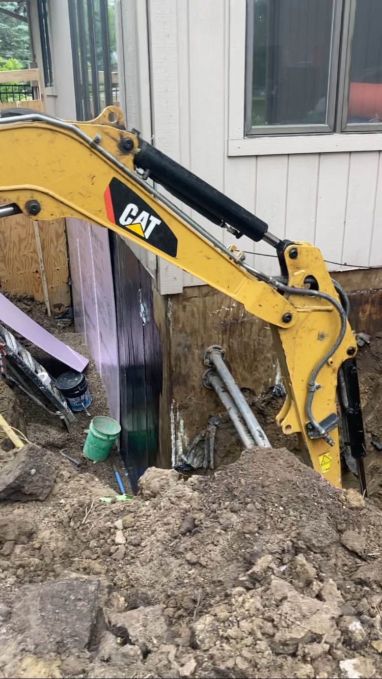 A yellow cat excavator is digging a hole in the ground in front of a house.