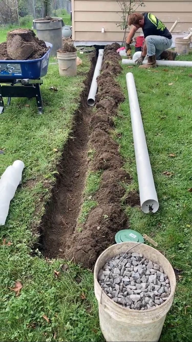 A man is working on a drainage system in a yard.