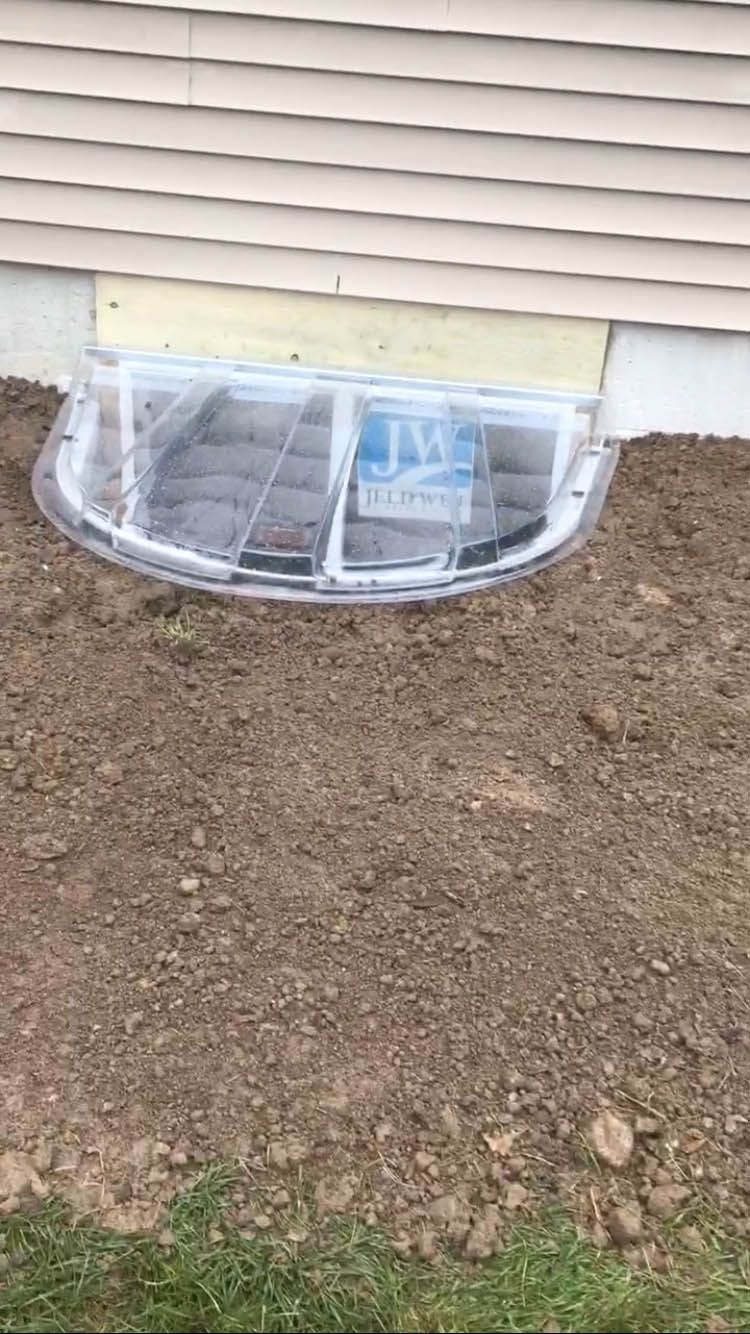 A window well in the ground next to a house.
