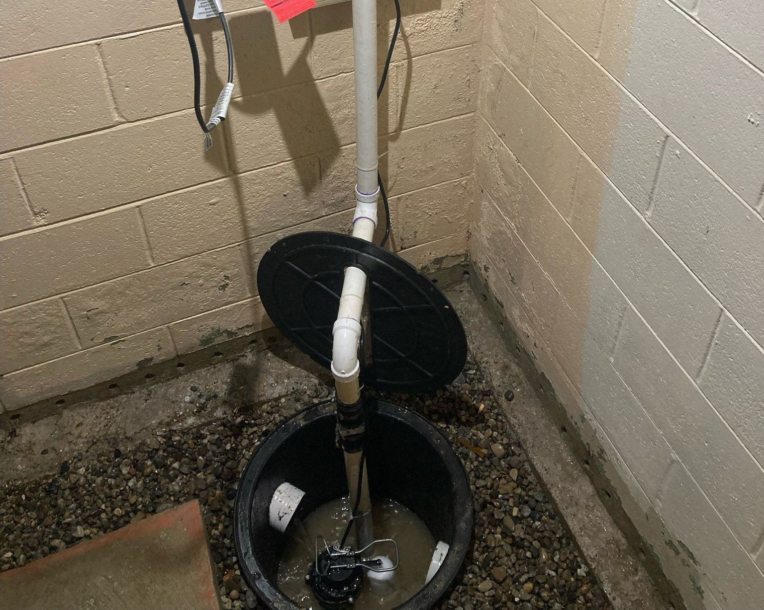 A sump pump is sitting in a basement next to a brick wall.