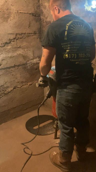 A man is standing in a basement using a vacuum cleaner.