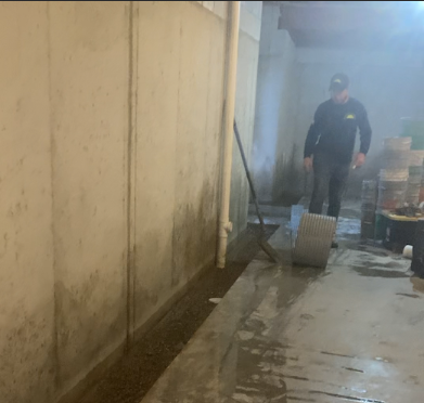 A man is standing in a dirty room with a broom