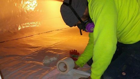 A man wearing a gas mask is cutting a roll of tape.