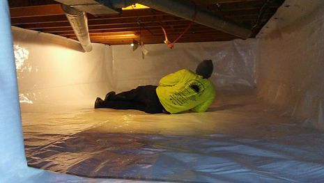 A man is laying on the floor of a basement covered in plastic.
