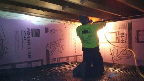 A man is kneeling down in a room with foam insulation on the wall.