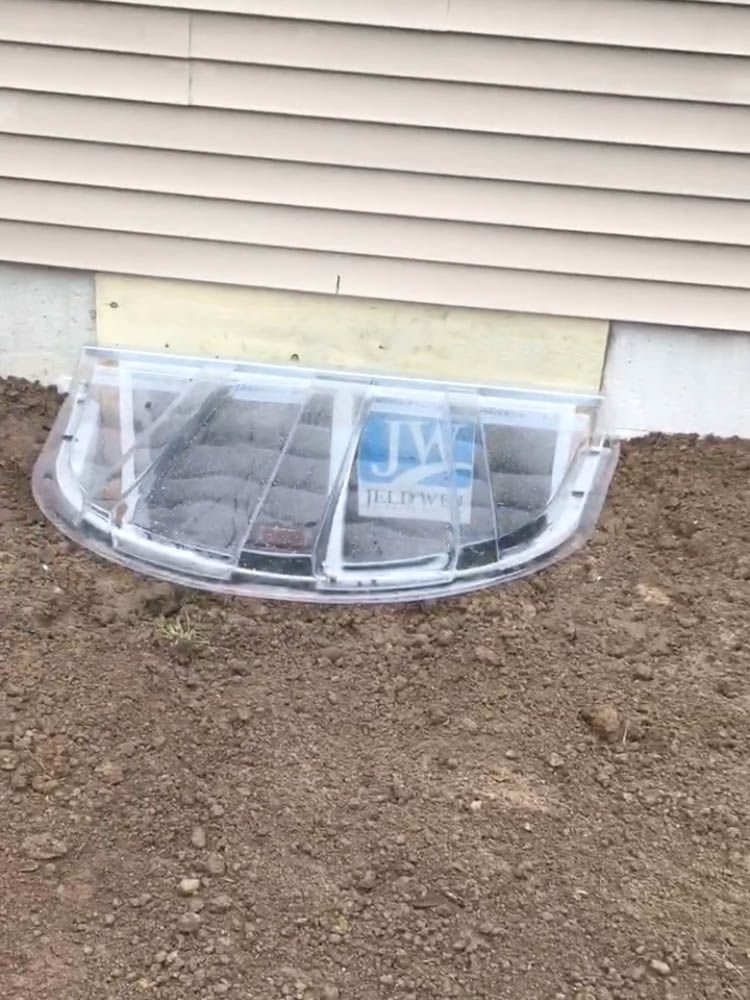 A window well in the ground next to a house.