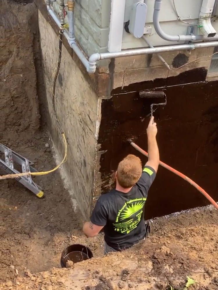 A man is painting a basement wall with a roller.