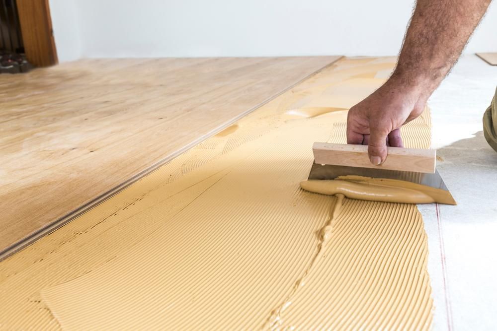 A Man Is Applying Glue To A Wooden Floor — Twin Towns Sand & Gravel In Tweed Heads South, NSW