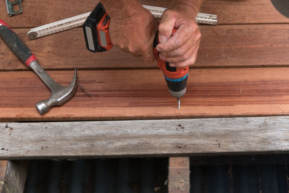 Close-up of hands using a cordless drill on a wooden deck in Chula Vista, CA.