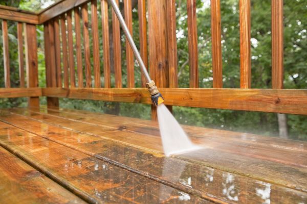 Power washing a wooden deck with a high-pressure hose, cleaning the wet surface.