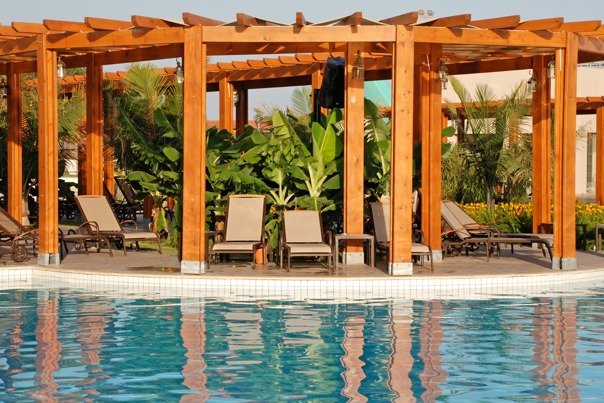 A photo of a pergola installed next to a pool. This is a luxury home and backyard and the pergola looks stunning sitting next to the pool