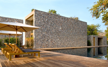 A luxurious photo of a pool deck installed in a modern home in California. The pool deck wraps completely around the pool, and on the left of the photo, there are lawn chairs with umbrellas for people to either rest in the shade or bath in the sun.