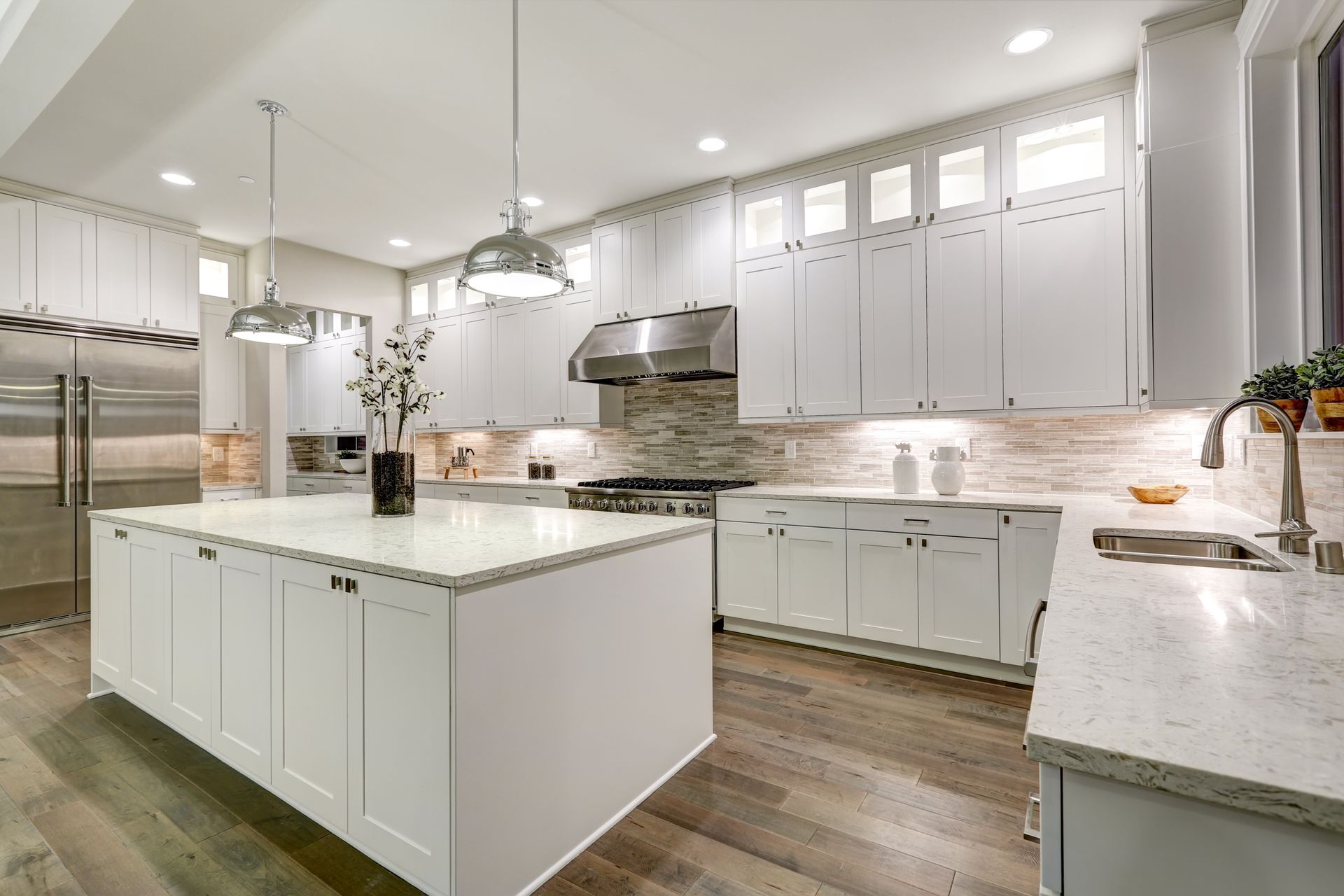 Modern white kitchen with an island, stainless steel appliances, and hardwood floors.