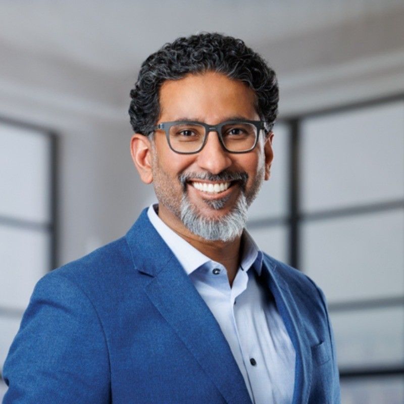 A man wearing glasses and a blue suit is smiling for the camera.
