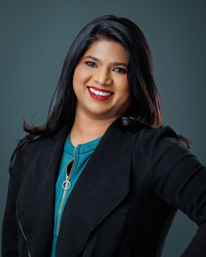 A woman wearing a black jacket and a blue shirt is smiling for the camera.