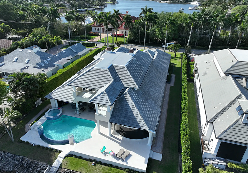 Two-story house with light blue siding and a light blue metal roof. White balconies and green trees surround the home.