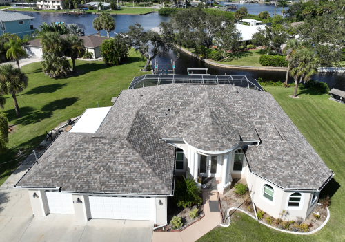 A beige-roofed house with a garage, set in a sunny, suburban area with palm trees and a lake.