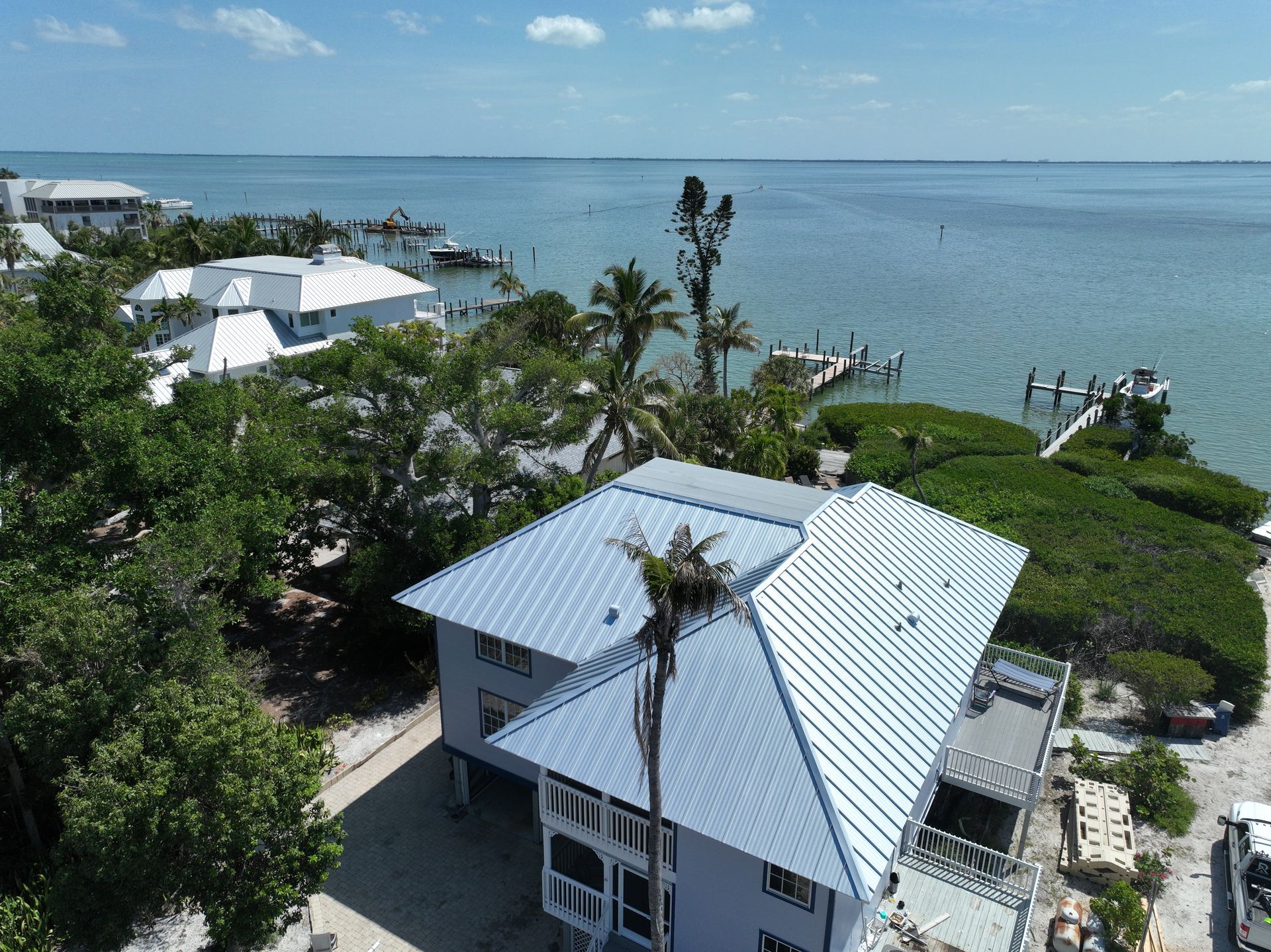 Aerial view of a coastal house with a silver roof, palm trees, and the ocean.