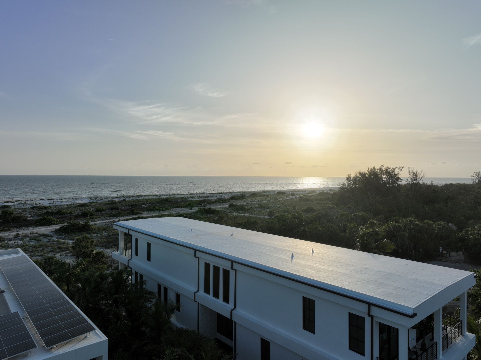 White buildings with solar panels, ocean view under setting sun.