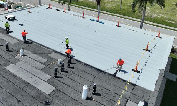 Roofers working on a flat roof with gray material and safety cones.