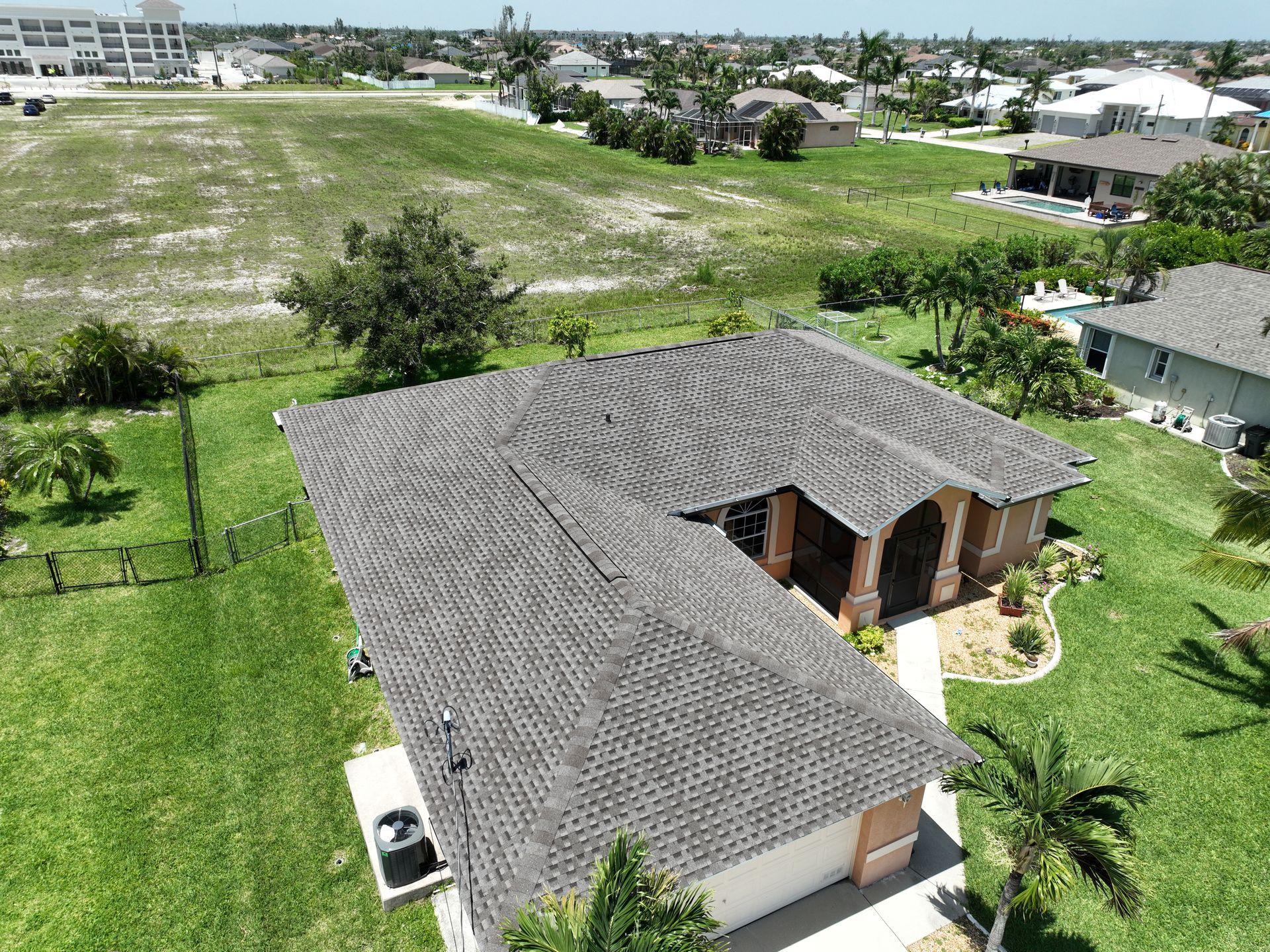 Aerial view of a gray-roofed house with green lawn, trees, and other houses nearby.