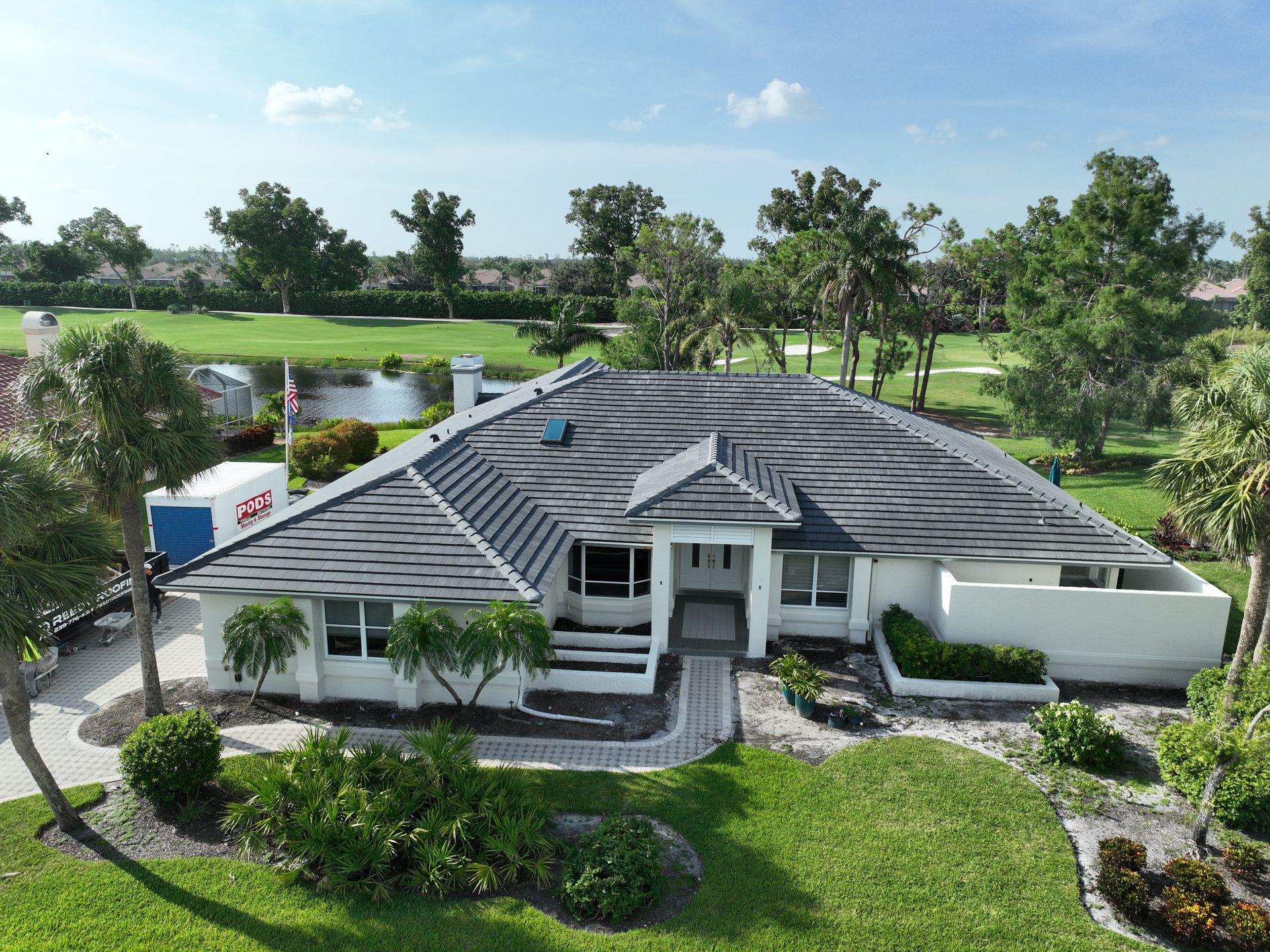 Aerial view of a white house with a dark gray roof, situated on a green lawn near a golf course.