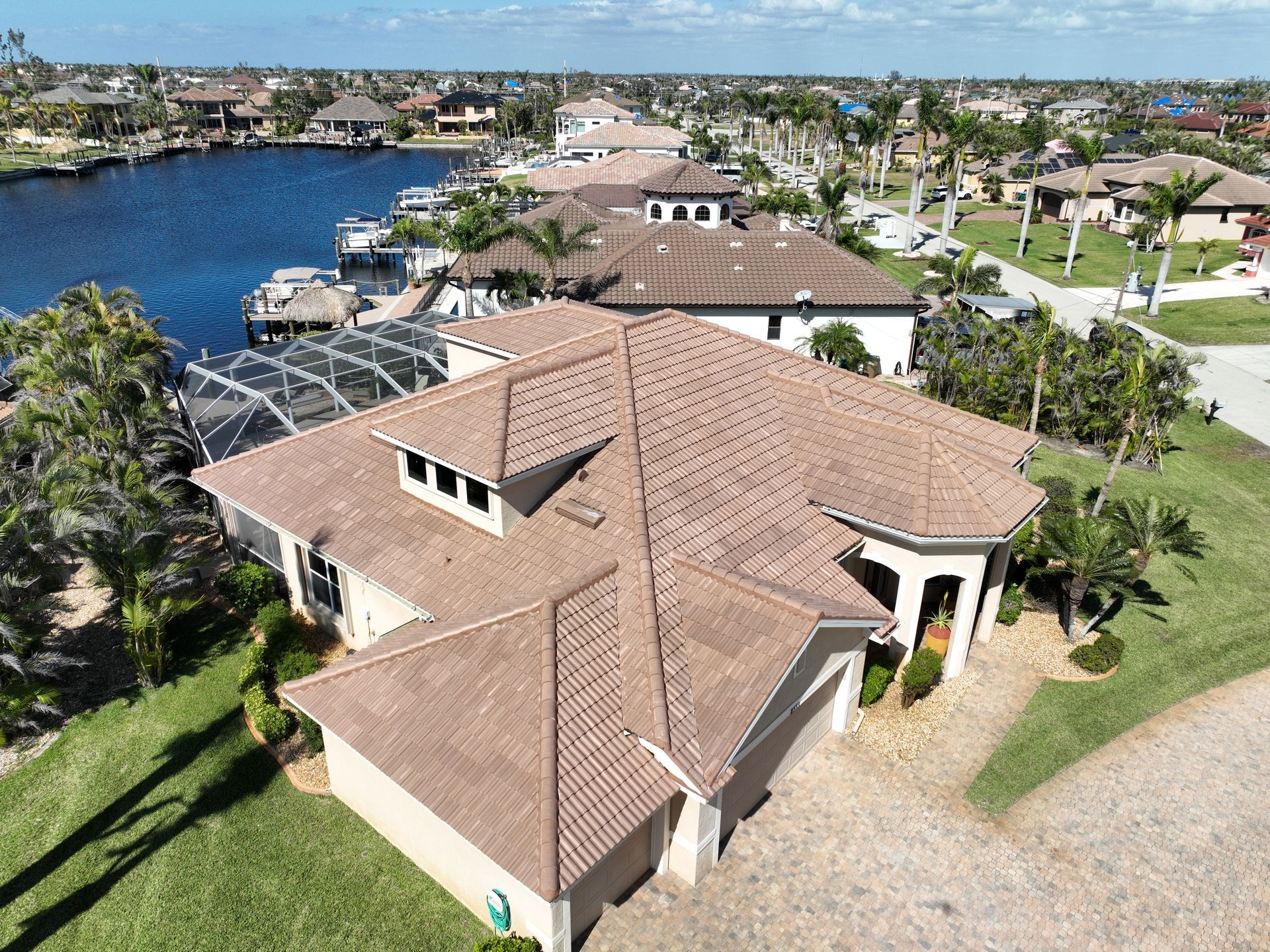 Aerial view of a home with a brown tiled roof, canal access, and surrounding palm trees.
