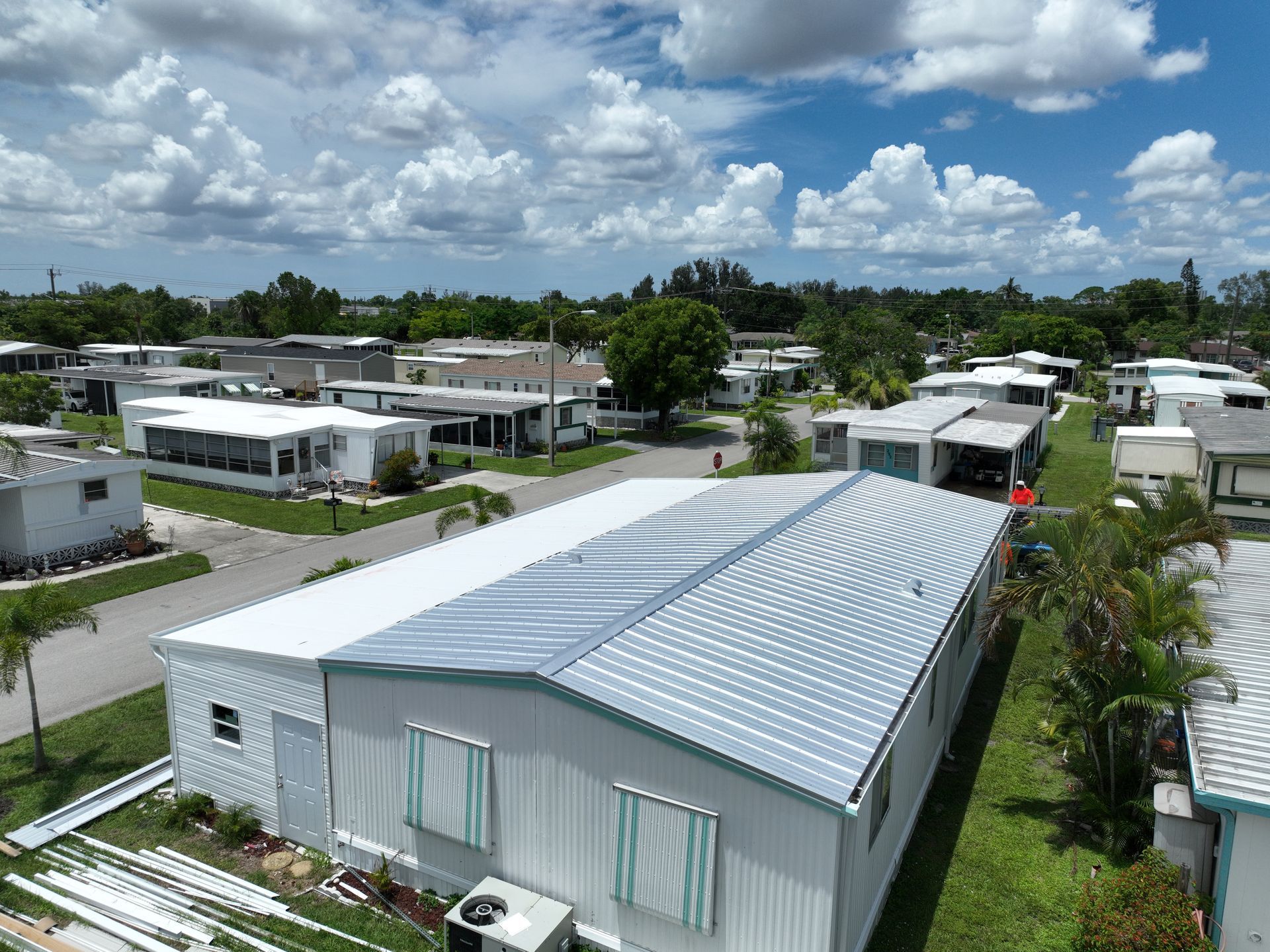 Aerial view of a mobile home park with white and gray homes under a cloudy blue sky.