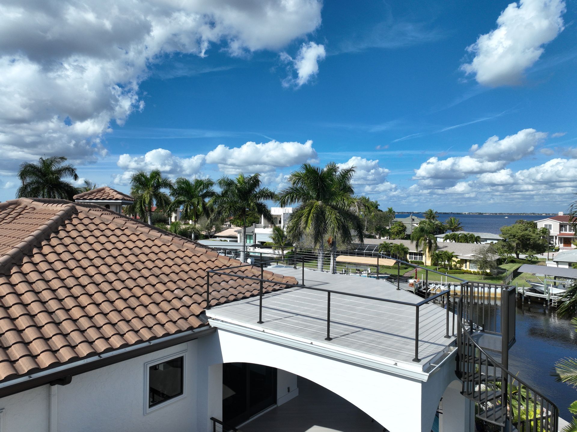 Rooftop view of houses with palm trees under a bright blue sky, overlooking water.