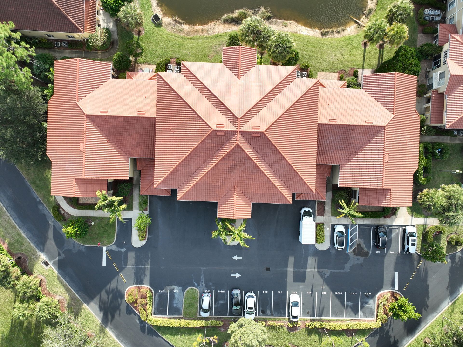 Aerial view of a building with red tiled roof, surrounded by parking and green landscaping.